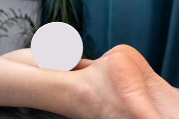 A jar of cream lies on the lower part of the women's legs. The heels are visible. Mockup for advertising. Selective focus.