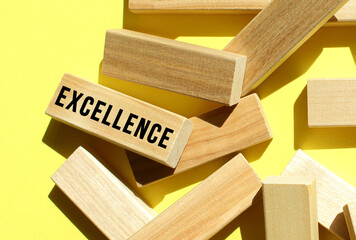 The EXCELLENCE text is written on one of the many scattered wooden blocks, against a yellow background.