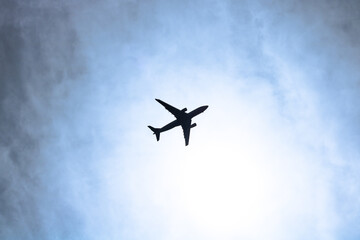 Silhouette of a plane on the cloudy sky background. Travel or vacation theme.
