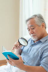 Asian senior old man longsighted , farsighted , reading a book with a magnifying glass on white...