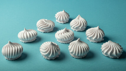 Beautifully laid out snow-white meringue cookies on a light turquoise background. Light dessert.
