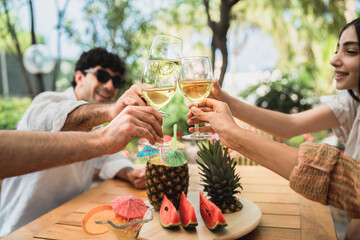 Group of young friends gathering on the terrace and having fun toasting to clinking wineglasses of white wine
