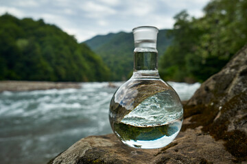 Bottle of drinking water on the shore of a mountain river.