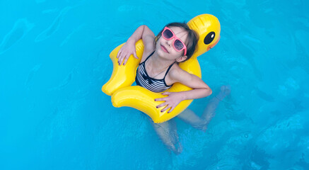 Cute girl in sunglasses swimming with rubber duck in swimming pool
