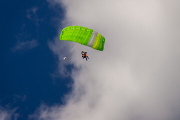 Skydiver under the canopy green of the parachute against a blue sky and white clouds