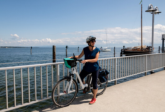 Frau mit Fahrrad auf Steg am Bodensee genießt bei wunderschönem Wetter Ihren Ausflug mit Fahrrad.