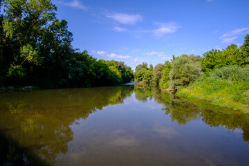 Fototapeta na wymiar Wide river water landscape on a green forest under a blue sunny sky