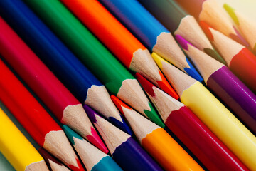 Colored sharpened pencils lie in a row close-up. Solid abstract background of wooden multi-colored pencils. These are school supplies.