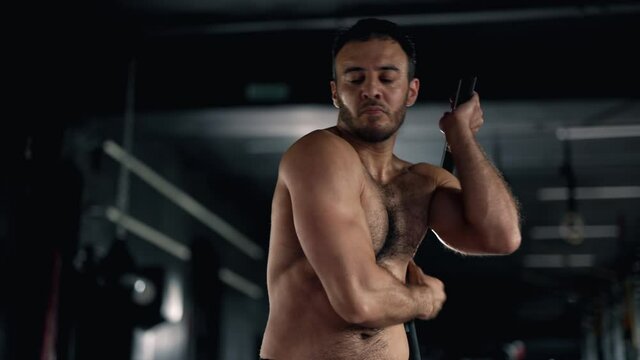 A muscular sportsman is doing exercise in the gym. Self confident man is holding nunchuck and practicing kung fu. Maximum focus and strength. Concept of martial arts health and sports.
