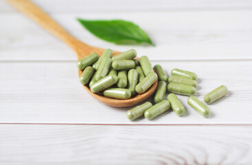 Andrographis paniculata capsule in wooden spoon on wooden background., Herbal extract medicine tablets pills.