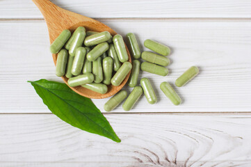 Andrographis paniculata capsule in wooden spoon on wooden background., Herbal extract medicine tablets pills.