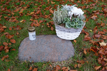 Steinplatte eines Rasengrabes mit Kerze und Blumenkorb im Herbst