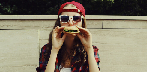 Portrait of happy young woman eating a burger fast food in the city