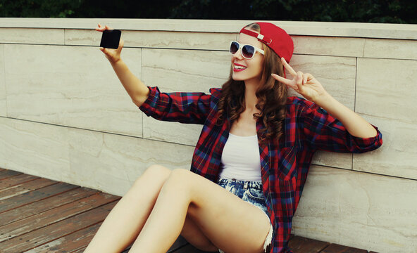 Portrait of teenager girl taking a selfie by smartphone wearing a baseball cap in the city
