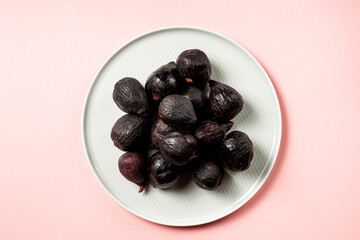 Fresh ripe figs in a plate. Beautiful blue violet fruit on pastel pink background. Healthy Mediterranean fig fruit. Copy space for text. Top view. Vegan concept
