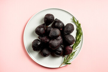 Fresh ripe figs in a plate. Beautiful blue violet fruit on pastel pink background. Healthy Mediterranean fig fruit. Copy space for text. Top view. Vegan concept