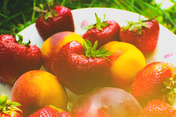 Strawberries and peaches on a plate on the green grass. Delicious and fresh summer fruits. Healthy vegetarian food with vitamins.