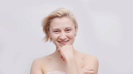 Fototapeta premium A beautiful blonde topless model with short hair posing for the camera. Hand on her chin smiling. Isolated girl over white background studio shot. Beauty concept.