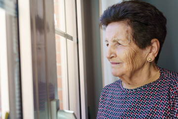 White 90 year old senior woman looking out the window thoughtfully.
