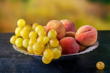 Ripe grapes and peaches in a metal bowl outdoors