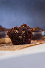 Selective focus on a healthy gluten free chocolate muffin with pecan nuts and cocoa powder. Homemade, freshly baked delicious cupcakes in the background on a wooden serving board. Nutrition concept