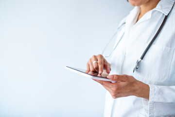 Cropped shot of a female doctor using a digital tablet. Close up of woman doctor hands using digital tablet at clinic. Closeup of female doctor in labcoat and stethoscope holding digital tablet