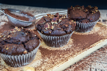 Healthy gluten free chocolate muffins with pecans on a wooden serving board. Homemade, freshly baked delicious cupcakes in baking cups with a crispy top and cocoa powder. Nutrition concept, side view