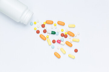Flat lay composition with bunch of different colorful pills scattered on table from popped plastic bottle. Pile of opened medication on white paper textured background. Close up, copy space for text
