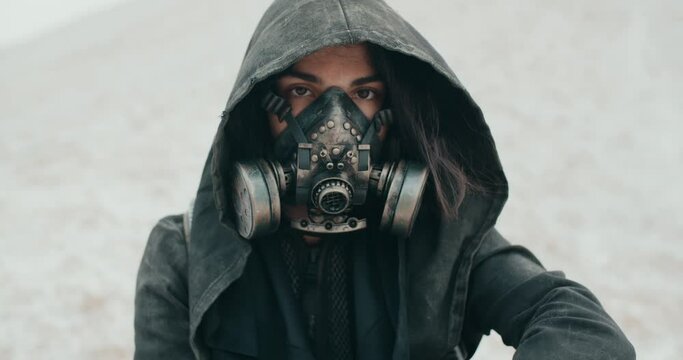 Portrait post apocalyptic brunette woman wearing grunge hooded mantle protective gas mask in desert. Steampunk cyberpunk wanderer. Stalker concept, future female survivor after nuclear war