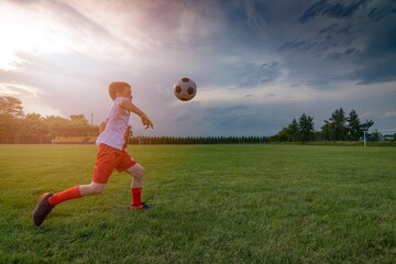 Naklejka premium Boy playing with football ball on playing field. Child playing football. White - red football kit.
