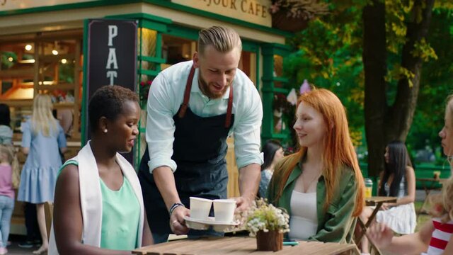 In the middle of park at coffee terrace group of multiethnic ladies enjoy the time together barista brings fresh coffee ladies takes the coffee and start to conversation they are smiling and feeling