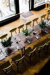 a large wooden table with serving, glasses, green rag napkins and compositions of fresh white flowers. View from above. A room with stone walls. Chandelier made of animal horns. holiday concept.