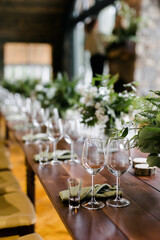 
wine glasses are in a row on a wooden table. a large table with serving and compositions of fresh flowers. Accommodation with stone walls. Chandelier made of animal horns. holiday concept.
