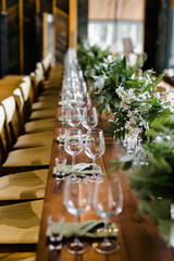 
wine glasses are in a row on a wooden table. a large table with serving and compositions of fresh flowers. Accommodation with stone walls. Chandelier made of animal horns. holiday concept.