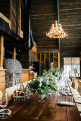 a large wooden table with serving, glasses, green rag napkins and compositions of fresh flowers. White flowers. A room with stone walls. Chandelier made of animal horns. holiday concept.