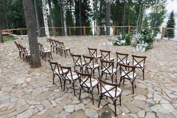 Obraz premium brown wooden chairs with cross-backs. Wedding decoration in nature, against the backdrop of the river and pine trees. natural wedding decor in a rustic style. holiday concept.