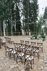 Fototapeta na wymiar brown wooden chairs with cross-backs. Wedding decoration in nature, against the backdrop of the river and pine trees. natural wedding decor in a rustic style. holiday concept.