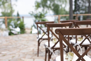 Fototapeta na wymiar brown wooden chairs with crisscross back. White pillows on chairs and envelopes with white rose petals. against the backdrop of nature on a stone floor. holiday concept.