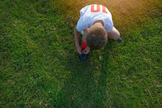 Little player is tying the shoelaces on the soccer field. Active lifestyle concept.