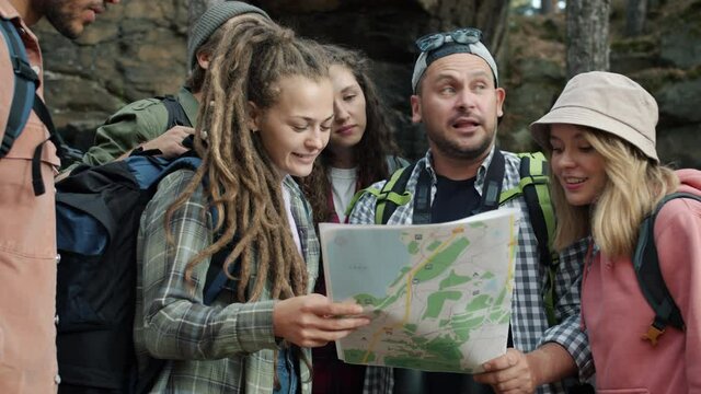 Cheerful friends tourists are studying map then walking in green autumn forest talking enjoying journey on foot. Tourism and active lifestyle concept.