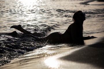 Young woman relaxing at the beach, lying on the sand in the sunset
