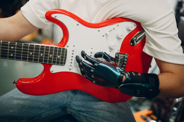 Young disabled man with artificial prosthetic hand plays on electric guitar at shop