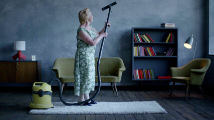 Happy elderly woman dancing with vacuum cleaner