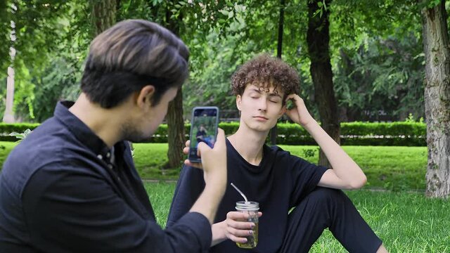 A guy takes pictures on the phone of another guy in nature in the summer