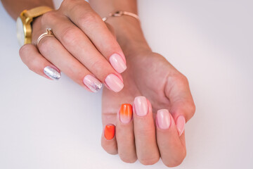 Hands of a young woman on a white background close-up. The nails are covered with a soft pink, orange gel polish with a gloss.