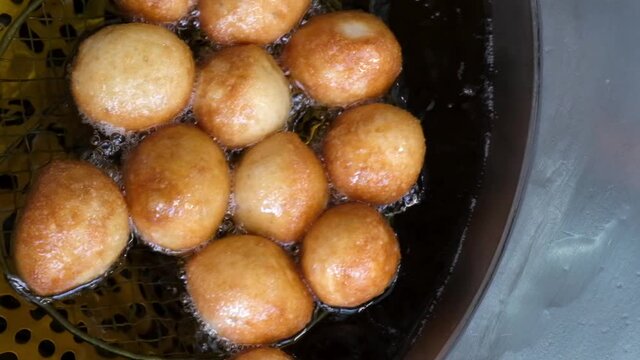 Slow motion of frying lokma dough in heated oil and mixing with sieve, traditional Greek sweet food, top down view