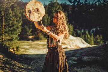 beautiful shamanic girl playing on shaman frame drum in the nature.
