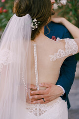 Obraz na płótnie Canvas Groom hugs bride in a white lace dress around the waist. Back view