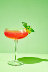 Watermelon cocktail with  cucumber slice and mint leaves in a coupe glass on a green. Minimalistic photo.