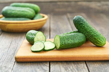Whole and sliced cucumbers on a cutting board, rustic style.